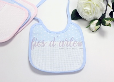 Babete para bebé azul com corações brancos e borda azul junto a rosas brancas.