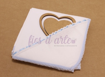 Toalha branca com borda azul e renda com coração de madeira ao fundo