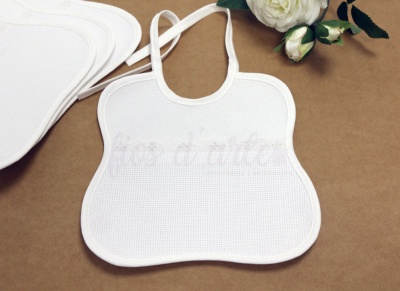 Babete branco de tecido com padrão de malha e flores artificiais em fundo castanho.