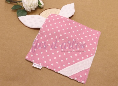 Lenço rosa com pintas brancas e orelhas brancas texturizadas sobre superfície castanha com flor e madeira