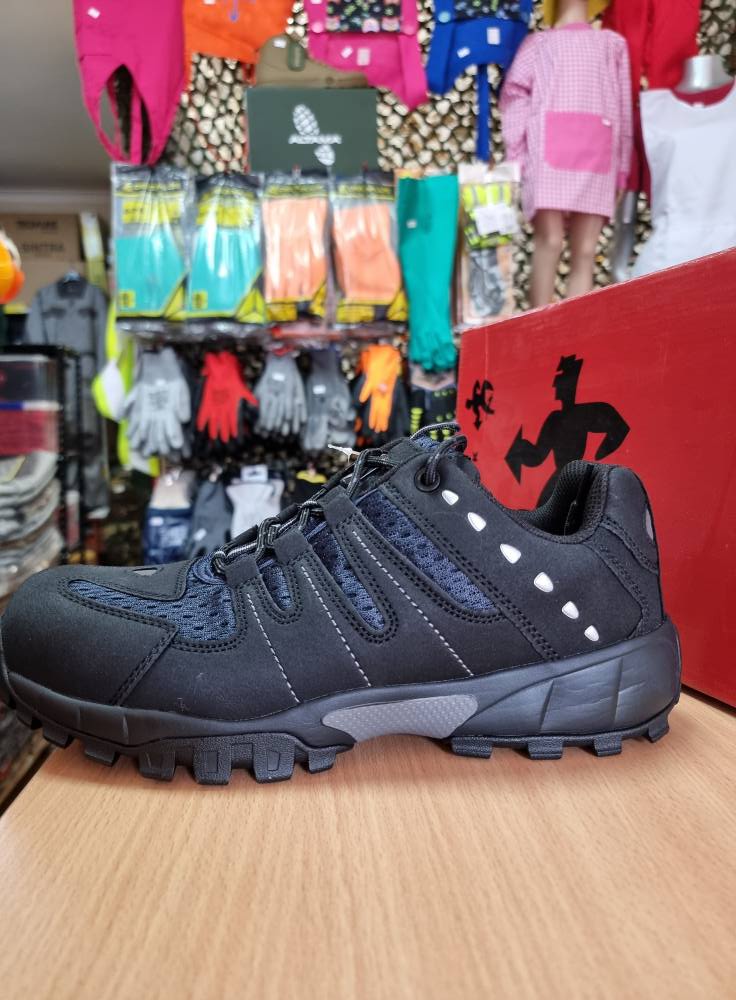 Ténis desportivo preto com detalhes em cinzento e branco sobre mesa de madeira