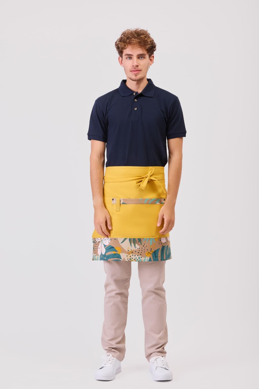 Homem com camisa polo azul escura, avental amarelo com padrão e calças bege