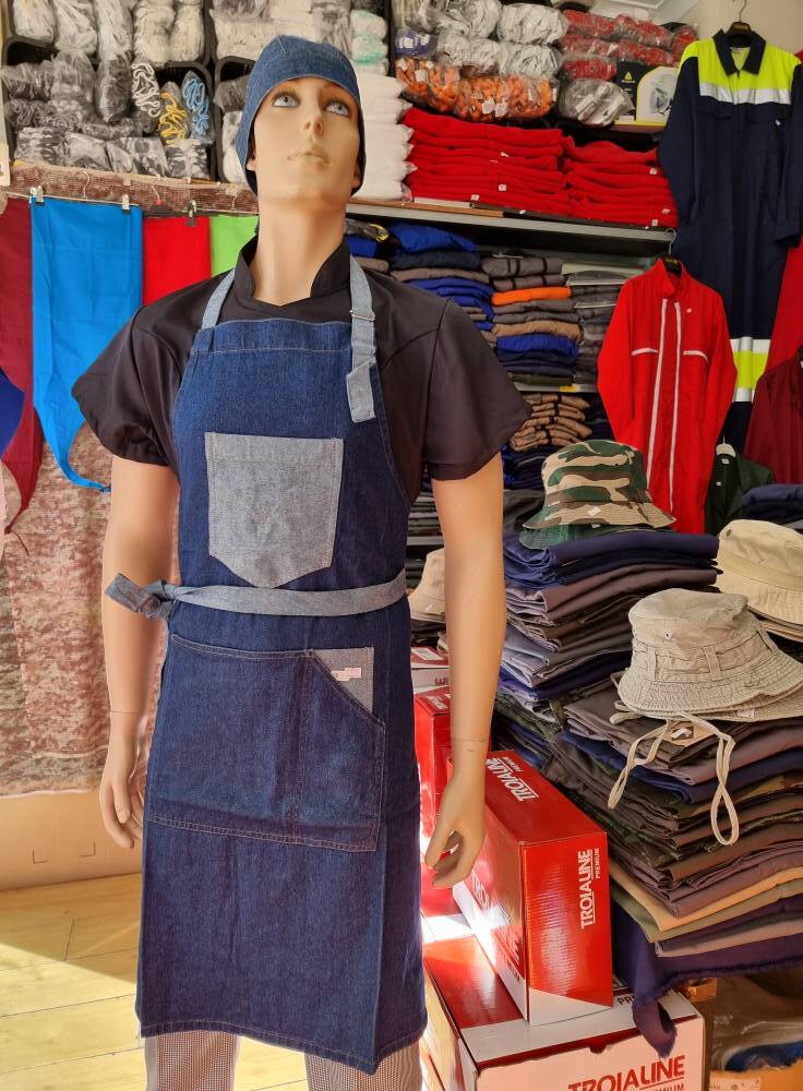 Maniquim com avental de ganga azul e touca, em loja com tecidos, roupas e chapéus