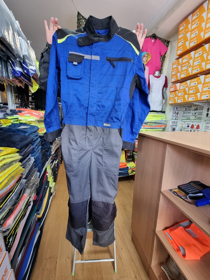 Macacão de trabalho azul e cinzento com bolsos e fecho de correr, em exposição numa loja de equipamentos de trabalho
