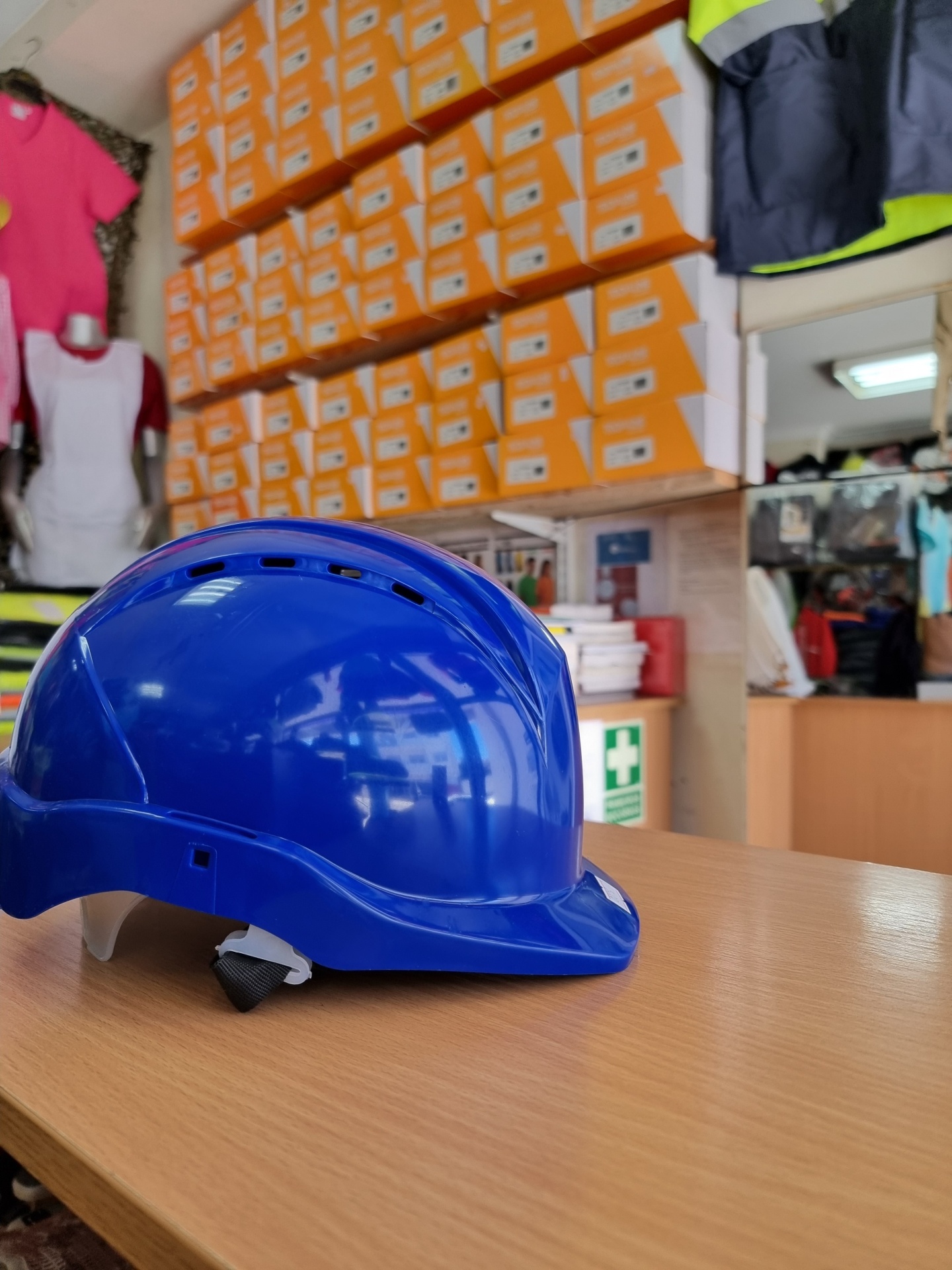 Capacete de segurança azul sobre mesa com caixas laranja ao fundo em loja.