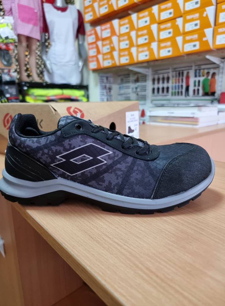 Ténis preto e cinzento com símbolo losango e sola branca sobre mesa de madeira