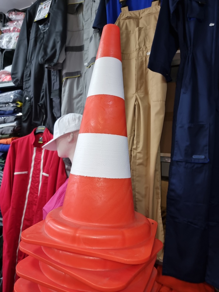 Cone de trânsito laranja com faixas brancas empilhado, com manequins e roupa de trabalho ao fundo