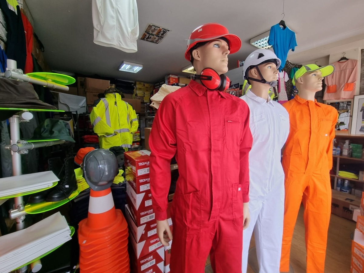 Três manequins com macacões coloridos e capacetes em loja de uniformes de trabalho