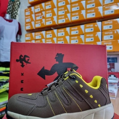 Sapatilha desportiva castanha com detalhes amarelos sobre caixa vermelha com logotipo