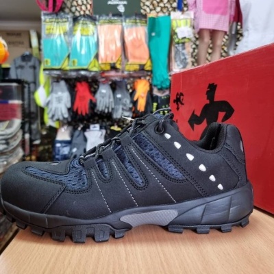 Ténis desportivo preto com detalhes em cinzento e branco sobre mesa de madeira