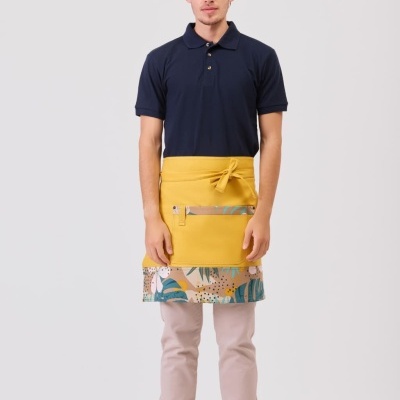 Homem com camisa polo azul escura, avental amarelo com padrão e calças bege