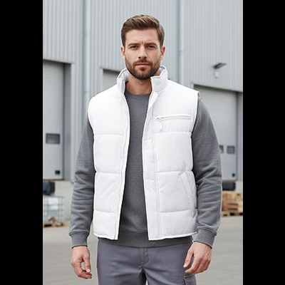 Homem com colete branco acolchoado e camisola cinzenta em ambiente industrial