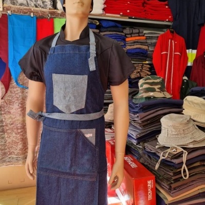 Maniquim com avental de ganga azul e touca, em loja com tecidos, roupas e chapéus