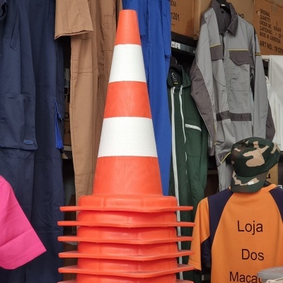 Cones de trânsito laranja com faixas brancas empilhados junto a macacões e t-shirt loja em fundo de armazém