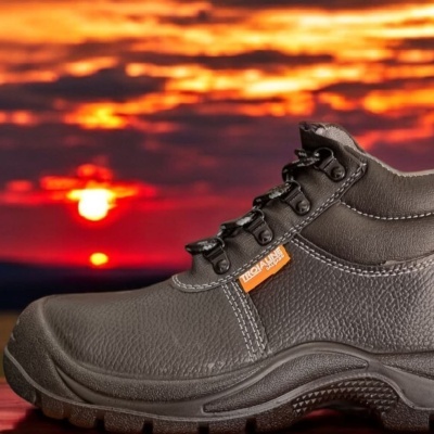 Bota de segurança preta com etiqueta laranja contra pôr do sol