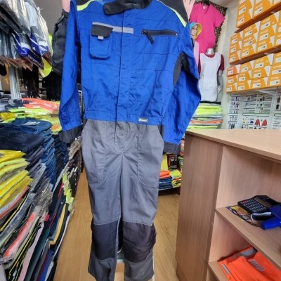Macacão de trabalho azul e cinzento com bolsos e fecho de correr, em exposição numa loja de equipamentos de trabalho