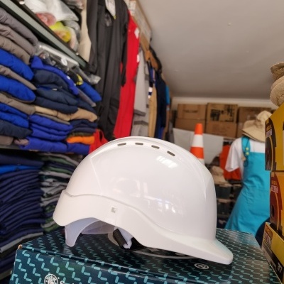 Capacete de segurança branco sobre caixa azul com roupas dobradas ao fundo