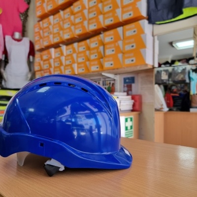 Capacete de segurança azul sobre mesa com caixas laranja ao fundo em loja.