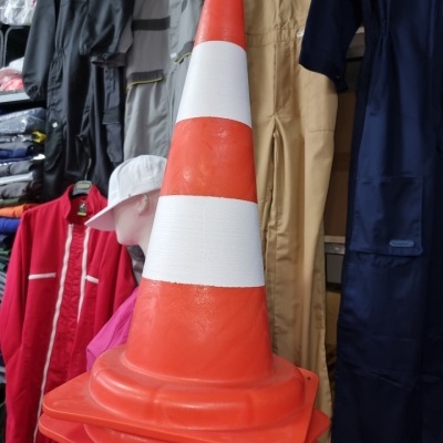 Cone de trânsito laranja com faixas brancas empilhado, com manequins e roupa de trabalho ao fundo
