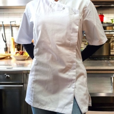 Bata de chef branca de manga curta com fecho cruzado e botões metálicos numa cozinha profissional