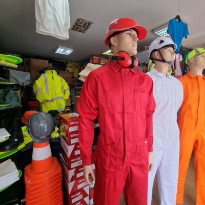 Três manequins com macacões coloridos e capacetes em loja de uniformes de trabalho