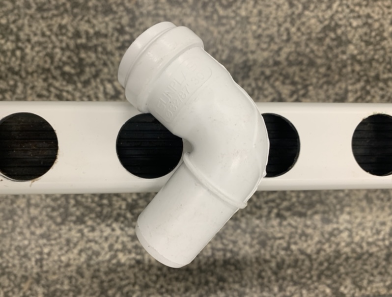 Joelho para Topos de Descarga - 2 mão Conector de tubo branco em PVC curvo colocado sobre suporte com círculos pretos