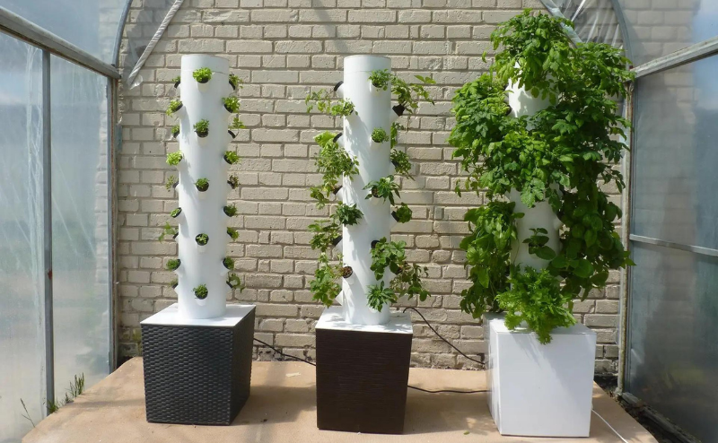 Três sistemas verticais de cultivo hidropónico com vasos quadrados e plantas verdes