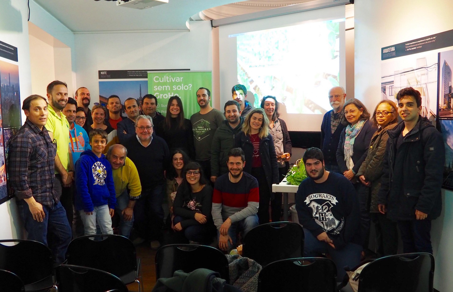 Fotografia de grupo em sala com cartaz verde 'Cultivar sem solo? É possível!' e cadeiras pretas