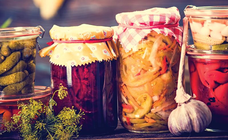 Frascos de vidro com legumes em conserva e tampas de tecido colorido sobre madeira