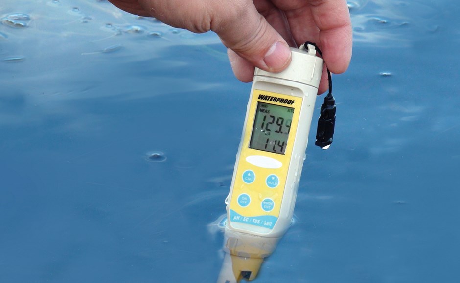 Medidor digital de pH à prova de água com visor digital e corpo amarelo e branco a ser segurado sobre água azul