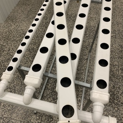 Estrutura hidropónica em PVC branco com tubos perfurados e suporte metálico