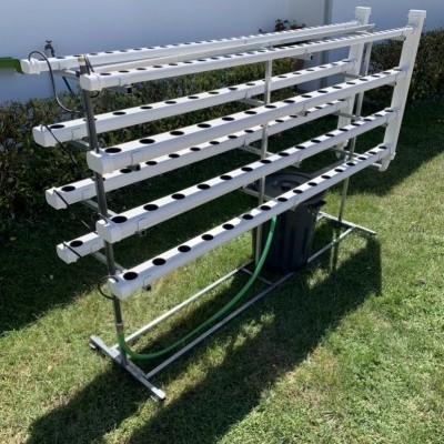 Sistema de cultivo hidropônico em tubos de PVC brancos em estrutura metálica ao ar livre