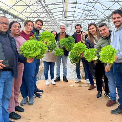 Grupo de pessoas em estufa segurando folhas de alface verde