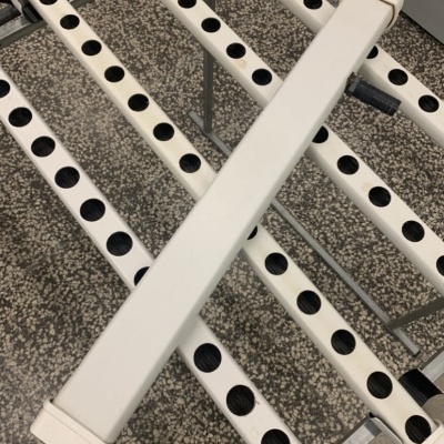 Estrutura tubular metálica branca com furos circulares pretos alinhados