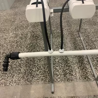 Tubo plástico branco com cabos pretos e suporte metálico sobre chão de mosaico