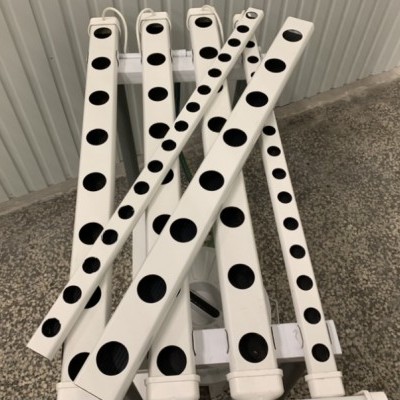 Tubos brancos com furos alinhados numa estrutura branca num chão cinzento rugoso