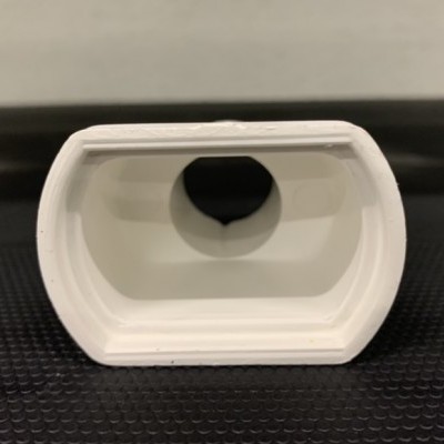 Peça de plástico branca com abertura oval e circular central preta sobre superfície preta