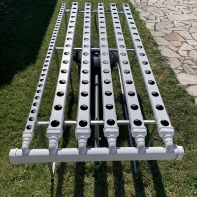 Sistema hidropônico com tubos brancos perfurados sobre suporte metálico na relva