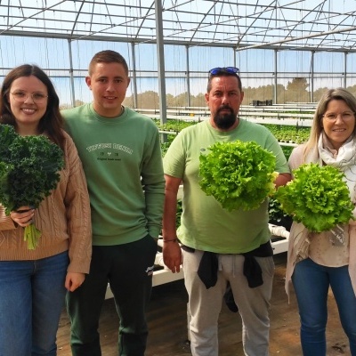 Quatro pessoas segurando alfaces verdes dentro de uma estufa hidropônica