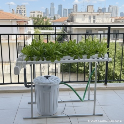 Sistema hidropónico com folhas verdes crescidas em tubos perfurados e depósito branco num terraço exterior.