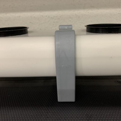 Suporte cinzento em tubo branco com bases pretas em fundo preto e parede clara