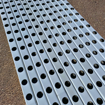 Barras metálicas prateadas com buracos circulares sobre chão de cascalho