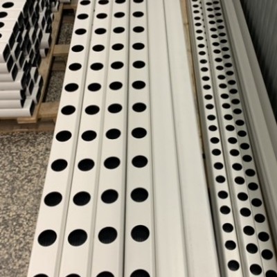Peças longas brancas de metal com furos redondos empilhadas num chão de pedra