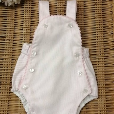 Macacão de bebé rosa claro com botões brancos sobre superfície de vime