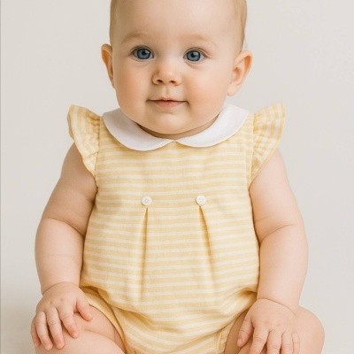 Bebé com macacão amarelo às riscas sentado em fundo neutro