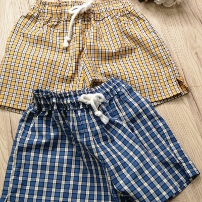 Dois calções de criança xadrez amarelo e azul com cordão branco sobre chão de madeira clara