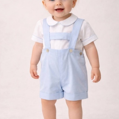 Bebé sorridente vestido com camisa branca e calção azul claro, calça sapatos brancos em fundo branco