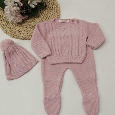 Conjunto de roupa de bebé rosa malha com camisola, calças com pés e gorro com pompom, arranjo de flores ao lado