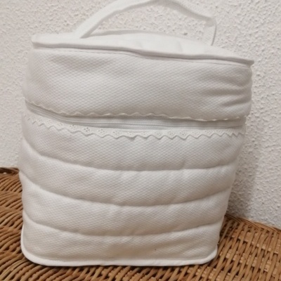 Bolsa branca acolchoada com fecho e pega sobre superfície de vime