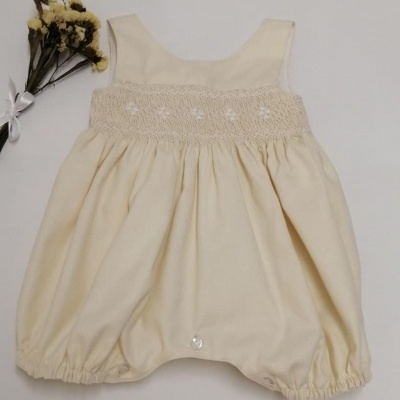 Macacão de bebé bege com bordado floral branco no peito e ramo de flores secas ao lado